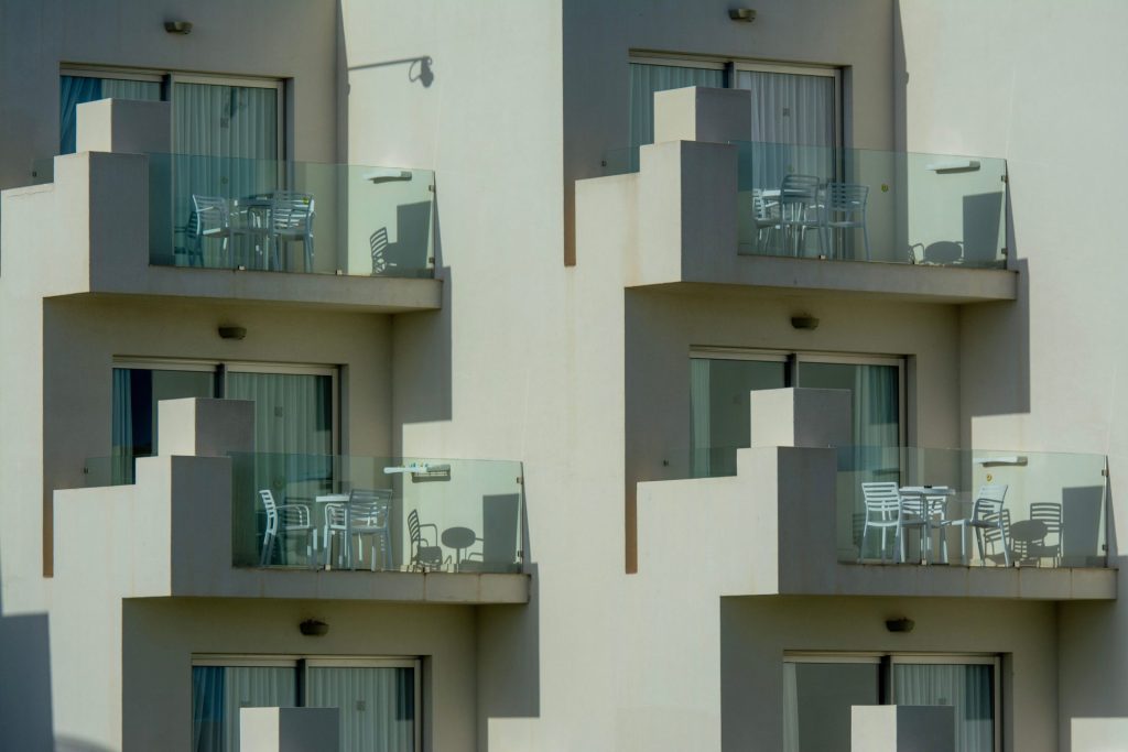 Architektonische Ansicht moderner Apartmentbalkone mit eleganten Glasgeländern und Gartenmöbeln.