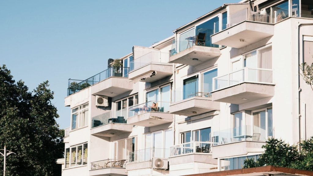 Modernes Apartmentgebäude mit Glasbalkonen und sommerlichem Ambiente.
