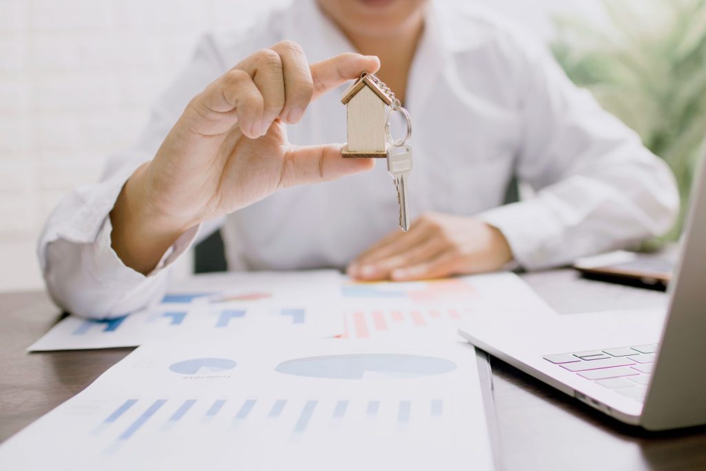 Ein Immobilienprofi präsentiert ein Hausmodell mit Schlüsseln, das die Immobilieninvestition und das Eigentum symbolisiert.