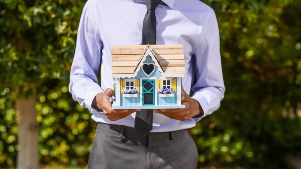 Ein Geschäftsmann hält ein dekoratives Miniaturhaus in der Hand, das Immobilieninvestitionen symbolisiert.